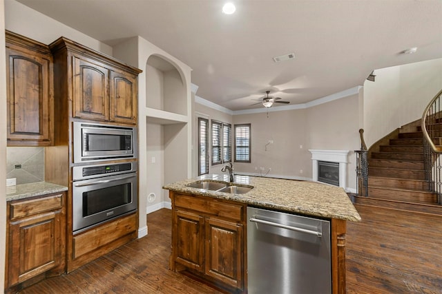 kitchen featuring sink, light stone counters, a center island with sink, ornamental molding, and stainless steel appliances