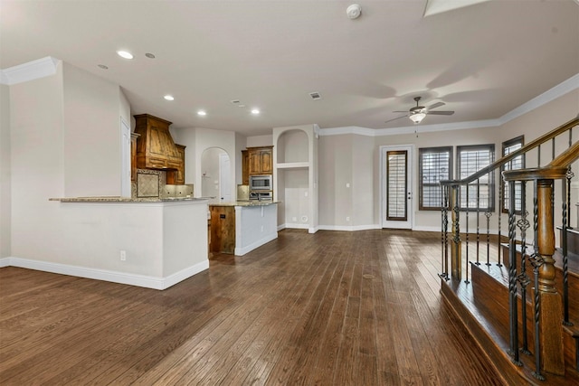 kitchen with stainless steel microwave, tasteful backsplash, ornamental molding, light stone countertops, and dark wood-type flooring