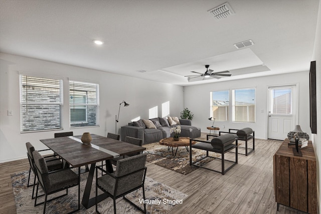 living room with ceiling fan, light hardwood / wood-style floors, and a tray ceiling