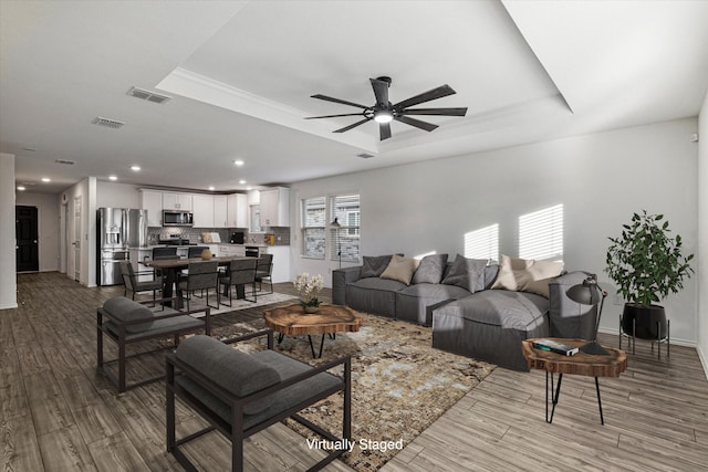 living room featuring a tray ceiling, light hardwood / wood-style flooring, and ceiling fan