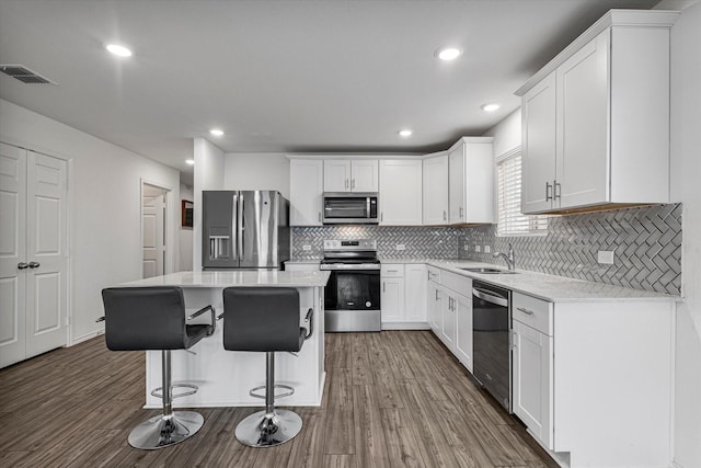 kitchen featuring a center island, hardwood / wood-style flooring, appliances with stainless steel finishes, tasteful backsplash, and white cabinetry