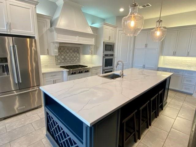 kitchen with pendant lighting, a kitchen island with sink, decorative backsplash, appliances with stainless steel finishes, and custom range hood