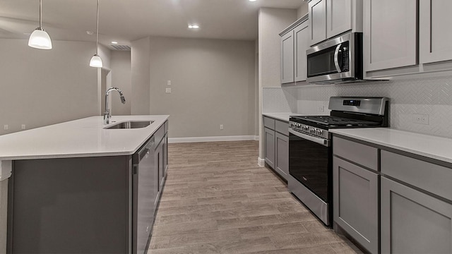 kitchen featuring gray cabinets, appliances with stainless steel finishes, a kitchen island with sink, and sink