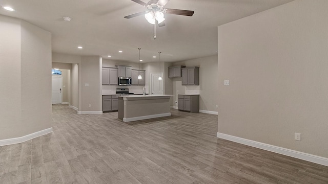 kitchen featuring hanging light fixtures, an island with sink, appliances with stainless steel finishes, and gray cabinetry