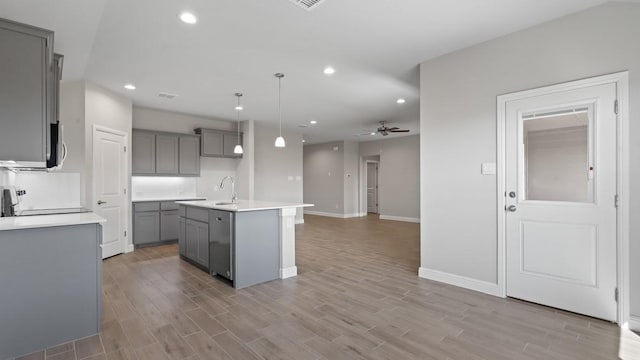 kitchen featuring pendant lighting, ceiling fan, an island with sink, and light wood-type flooring