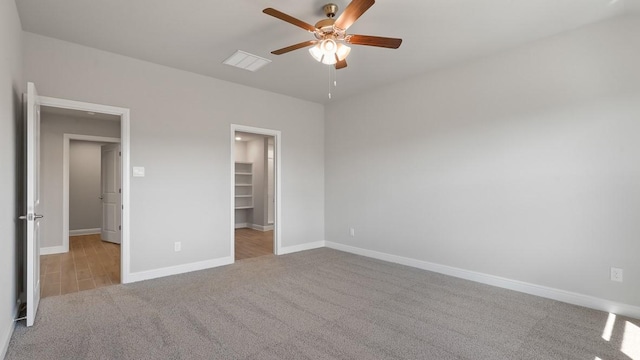 unfurnished bedroom with a spacious closet, light colored carpet, and ceiling fan