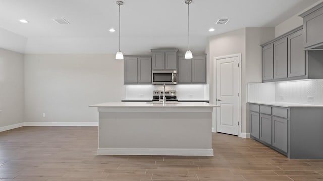 kitchen featuring decorative backsplash, stainless steel appliances, gray cabinetry, and an island with sink