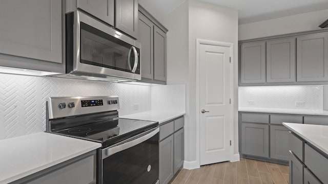 kitchen with stainless steel appliances, gray cabinets, light hardwood / wood-style floors, and backsplash