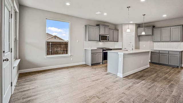 kitchen with a center island with sink, light hardwood / wood-style floors, decorative light fixtures, and appliances with stainless steel finishes