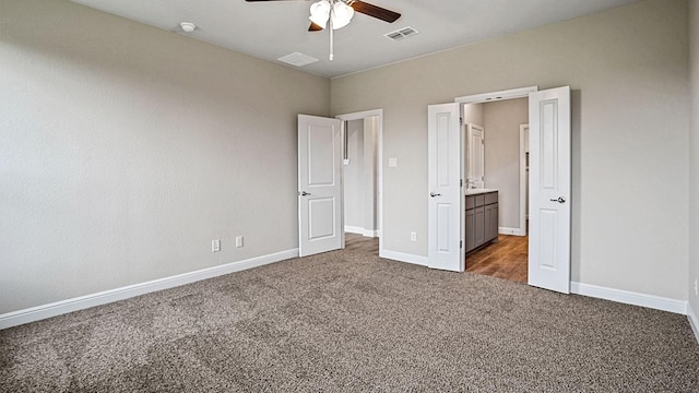 unfurnished bedroom with ceiling fan, ensuite bathroom, and dark colored carpet