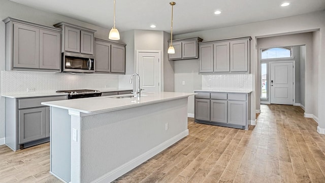 kitchen featuring gray cabinetry, sink, appliances with stainless steel finishes, and an island with sink