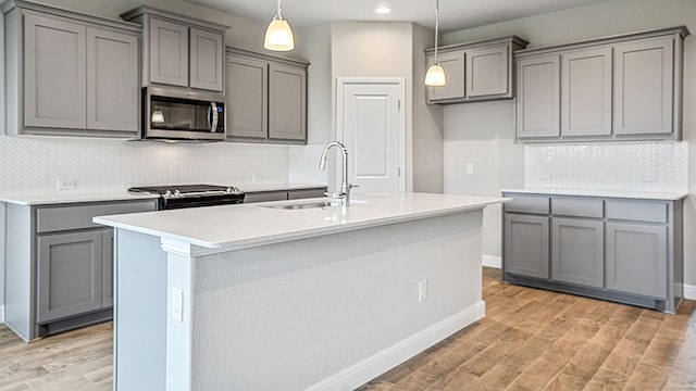 kitchen featuring gray cabinets, sink, stainless steel appliances, and an island with sink