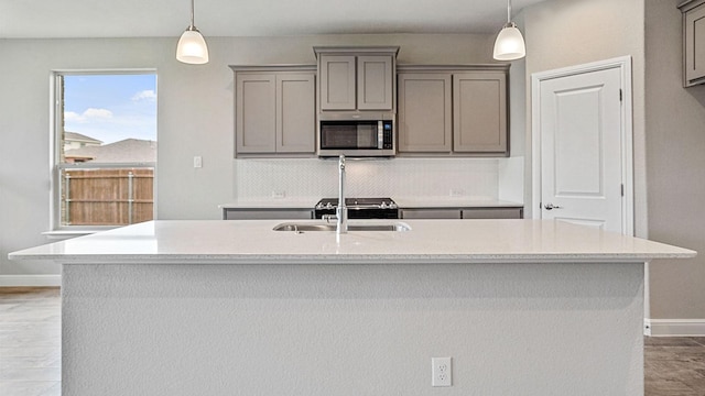 kitchen featuring a center island with sink, decorative light fixtures, and gray cabinets