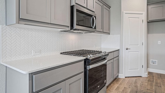 kitchen with light stone countertops, stainless steel appliances, light hardwood / wood-style flooring, gray cabinets, and decorative backsplash