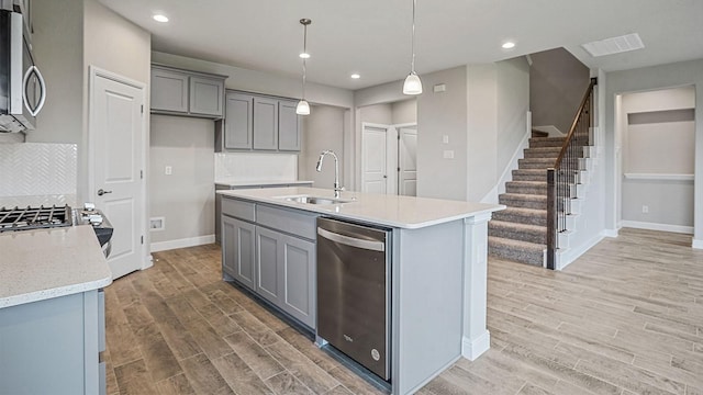 kitchen featuring sink, hanging light fixtures, stainless steel appliances, backsplash, and an island with sink