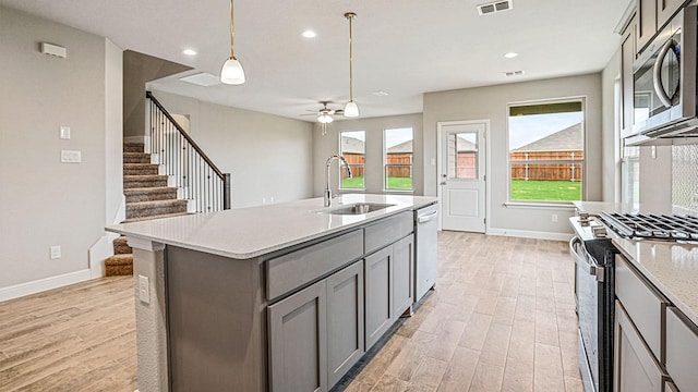 kitchen featuring stainless steel appliances, gray cabinets, a kitchen island with sink, and sink