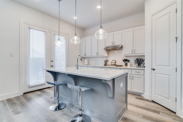 kitchen with tasteful backsplash, white cabinetry, a center island with sink, and pendant lighting