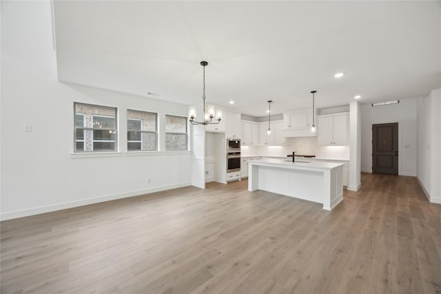 kitchen with appliances with stainless steel finishes, decorative light fixtures, white cabinetry, sink, and a kitchen island with sink