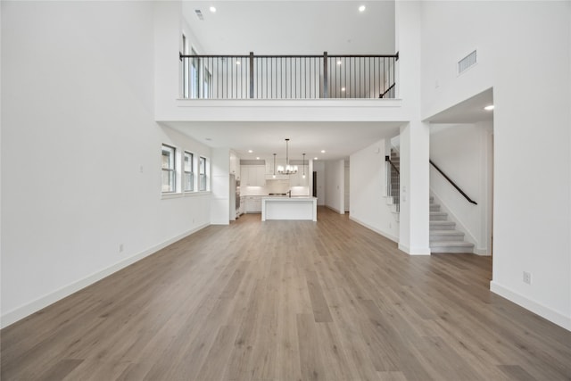 unfurnished living room featuring a high ceiling, a chandelier, and light wood-type flooring