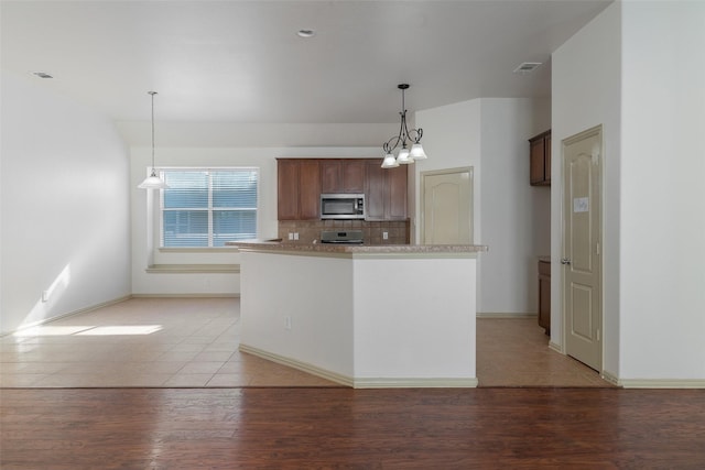 kitchen featuring pendant lighting, stove, backsplash, light hardwood / wood-style flooring, and a chandelier