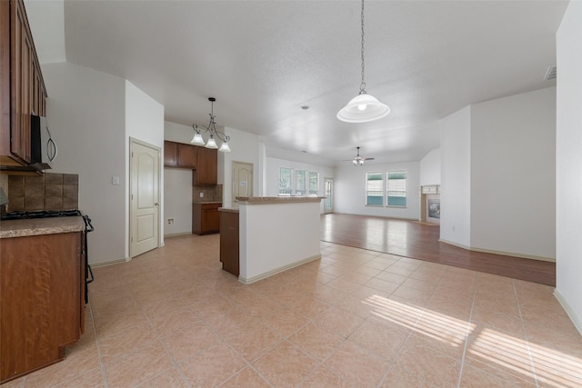 kitchen featuring stove, ceiling fan with notable chandelier, light tile patterned floors, tasteful backsplash, and decorative light fixtures