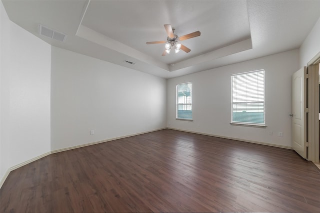 unfurnished room featuring dark hardwood / wood-style floors, ceiling fan, and a tray ceiling