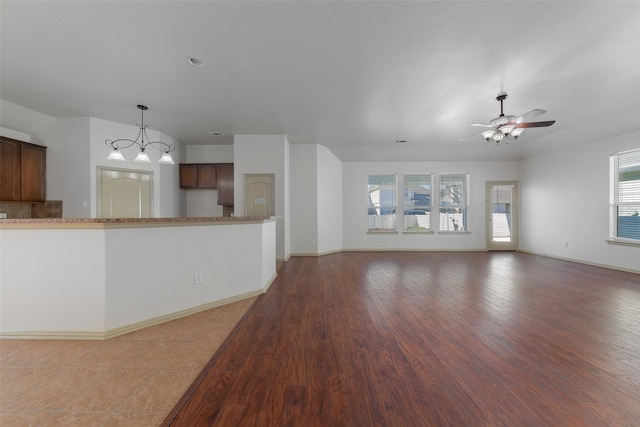 unfurnished living room featuring ceiling fan with notable chandelier and hardwood / wood-style flooring