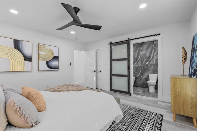 bedroom with a barn door, ensuite bathroom, ceiling fan, and light hardwood / wood-style floors