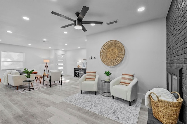 living room with ceiling fan, a fireplace, and light hardwood / wood-style floors