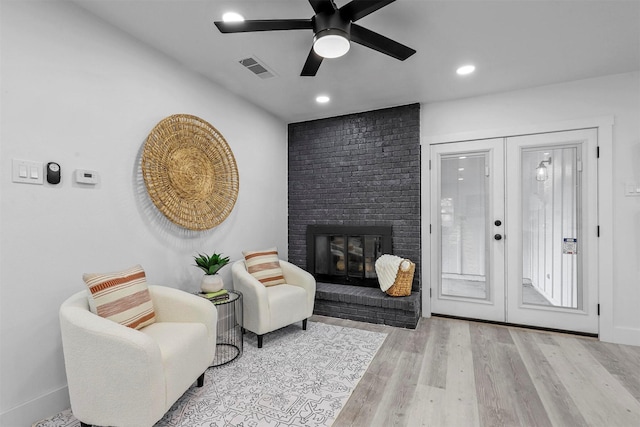 living room with a brick fireplace, ceiling fan, light hardwood / wood-style flooring, and french doors