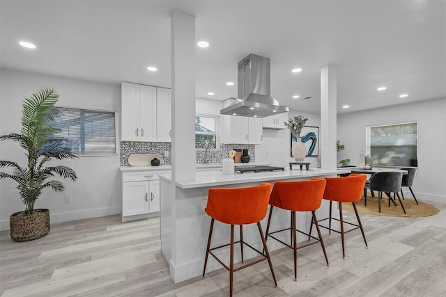 kitchen featuring backsplash, island exhaust hood, light hardwood / wood-style floors, a breakfast bar, and white cabinets