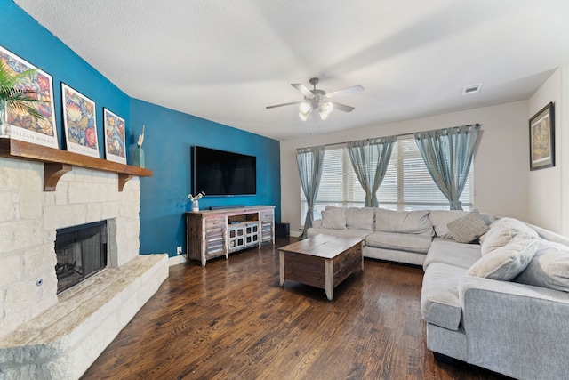 living room with a stone fireplace, dark wood-type flooring, a textured ceiling, and ceiling fan