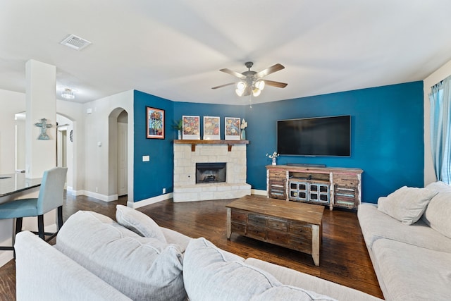 living room with ceiling fan, dark hardwood / wood-style flooring, and a stone fireplace