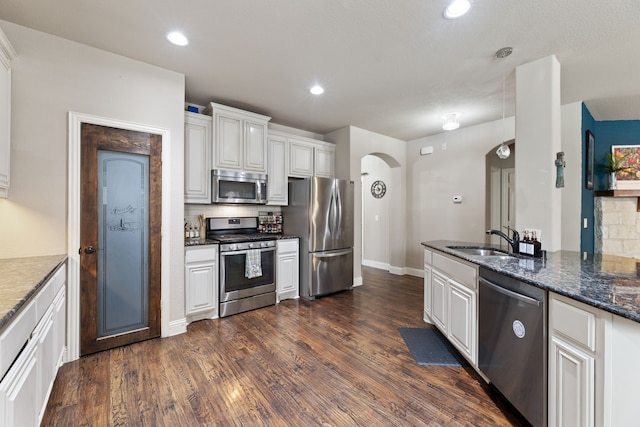 kitchen with appliances with stainless steel finishes, sink, dark stone countertops, and white cabinets