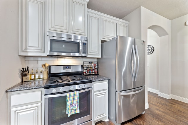 kitchen featuring stainless steel appliances, dark stone countertops, white cabinets, and backsplash