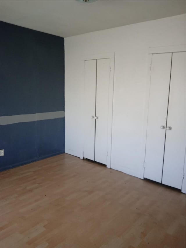 unfurnished bedroom with two closets and light wood-type flooring