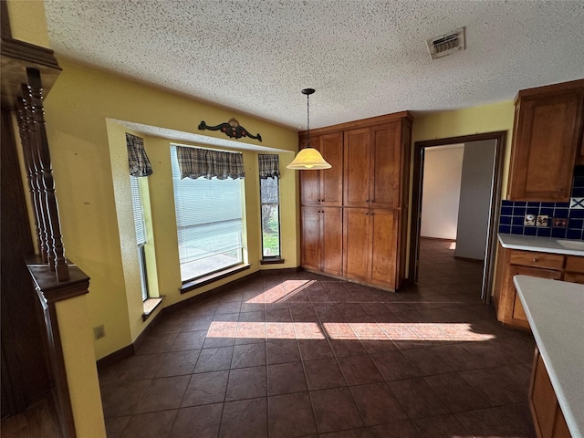 interior space featuring decorative light fixtures, dark tile patterned flooring, decorative backsplash, and a textured ceiling