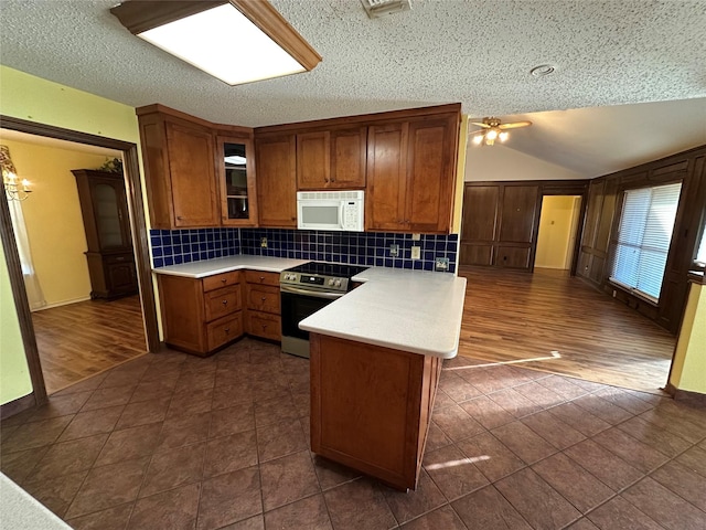 kitchen with lofted ceiling, stainless steel electric range, dark tile patterned flooring, decorative backsplash, and kitchen peninsula