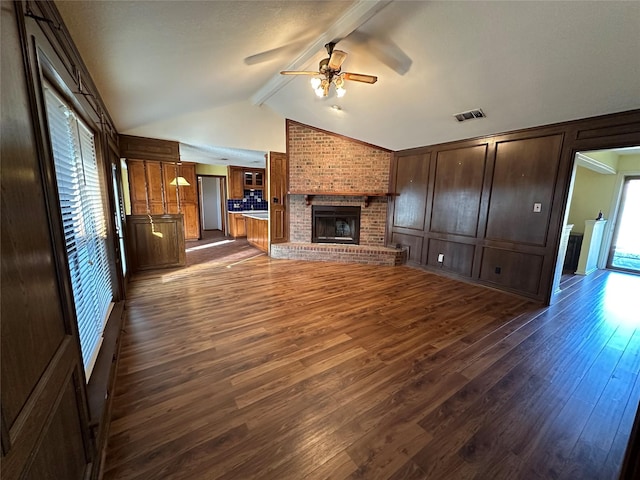 unfurnished living room with ceiling fan, dark hardwood / wood-style floors, a brick fireplace, and vaulted ceiling with beams