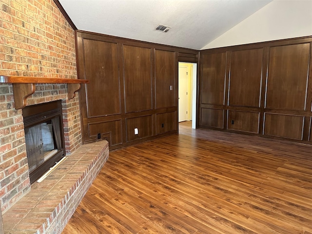 unfurnished living room featuring lofted ceiling, dark hardwood / wood-style floors, wooden walls, and a fireplace