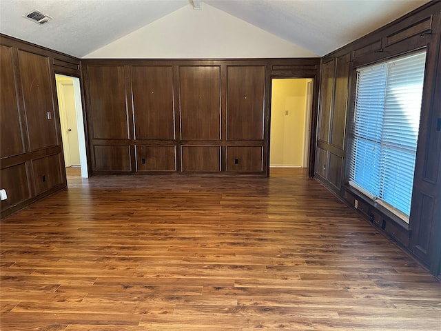 unfurnished bedroom featuring wooden walls, lofted ceiling, and dark hardwood / wood-style flooring