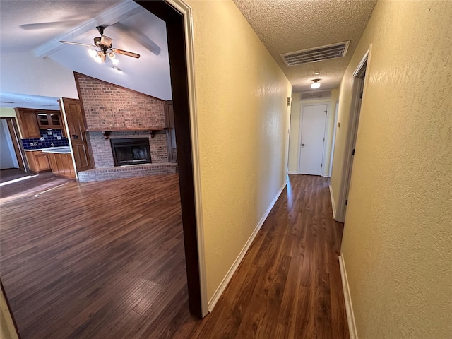 hall featuring lofted ceiling with beams, dark hardwood / wood-style floors, and a textured ceiling