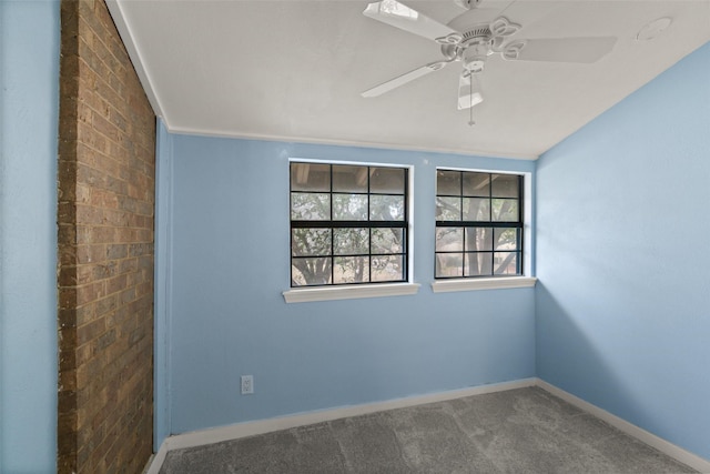 carpeted empty room featuring ceiling fan and brick wall