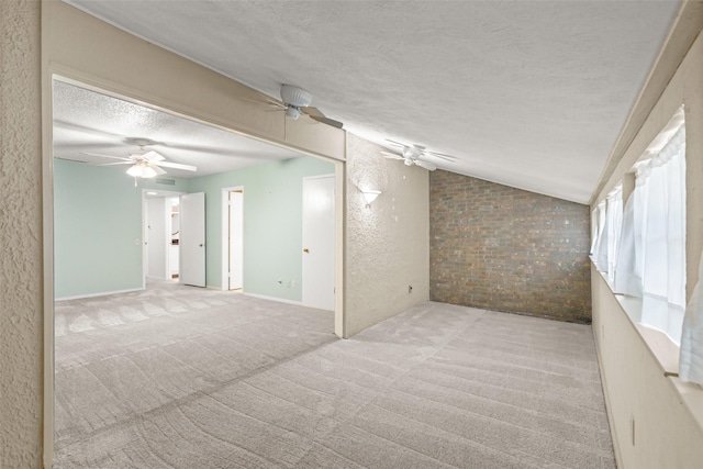 unfurnished room featuring lofted ceiling, ceiling fan, a textured ceiling, brick wall, and light colored carpet