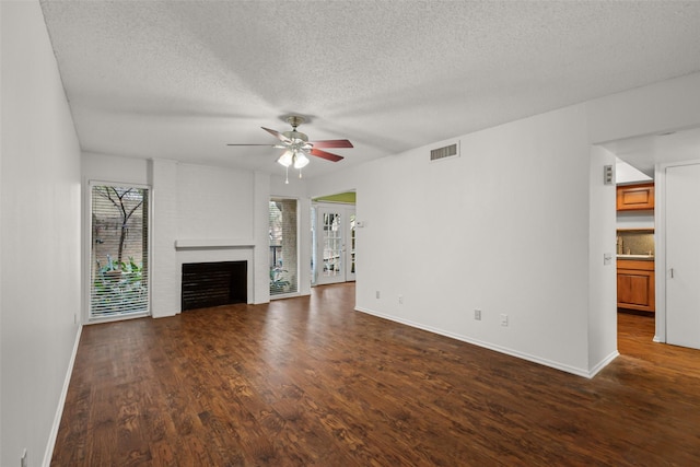 unfurnished living room with ceiling fan, a fireplace, dark hardwood / wood-style flooring, and a textured ceiling