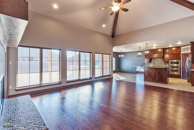 unfurnished living room featuring high vaulted ceiling, ceiling fan with notable chandelier, and light hardwood / wood-style flooring