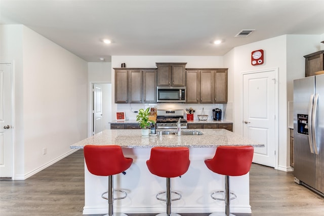 kitchen with a center island with sink, backsplash, light stone counters, and stainless steel appliances