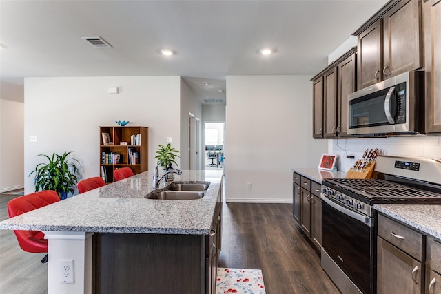 kitchen with a center island with sink, light stone countertops, sink, and appliances with stainless steel finishes