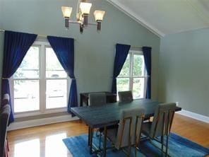 dining space with hardwood / wood-style floors, lofted ceiling, and a notable chandelier