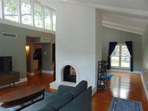 living room with beamed ceiling, high vaulted ceiling, hardwood / wood-style floors, and a fireplace